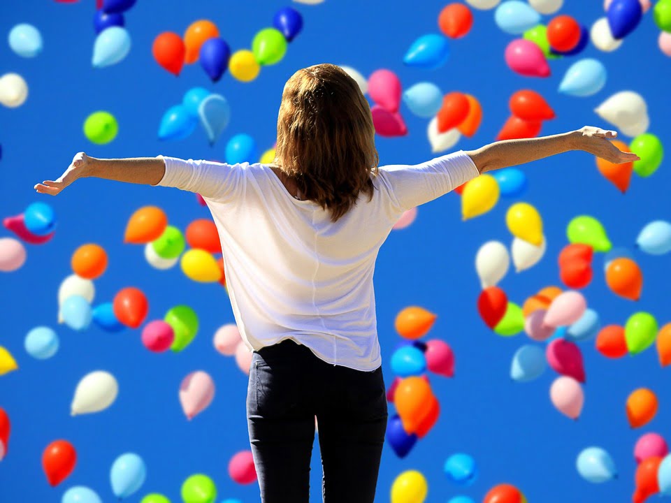 A girl enjoys life under blue balloons in the sky
